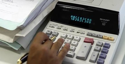 Pessoa fazendo contas em calculadora de mesa